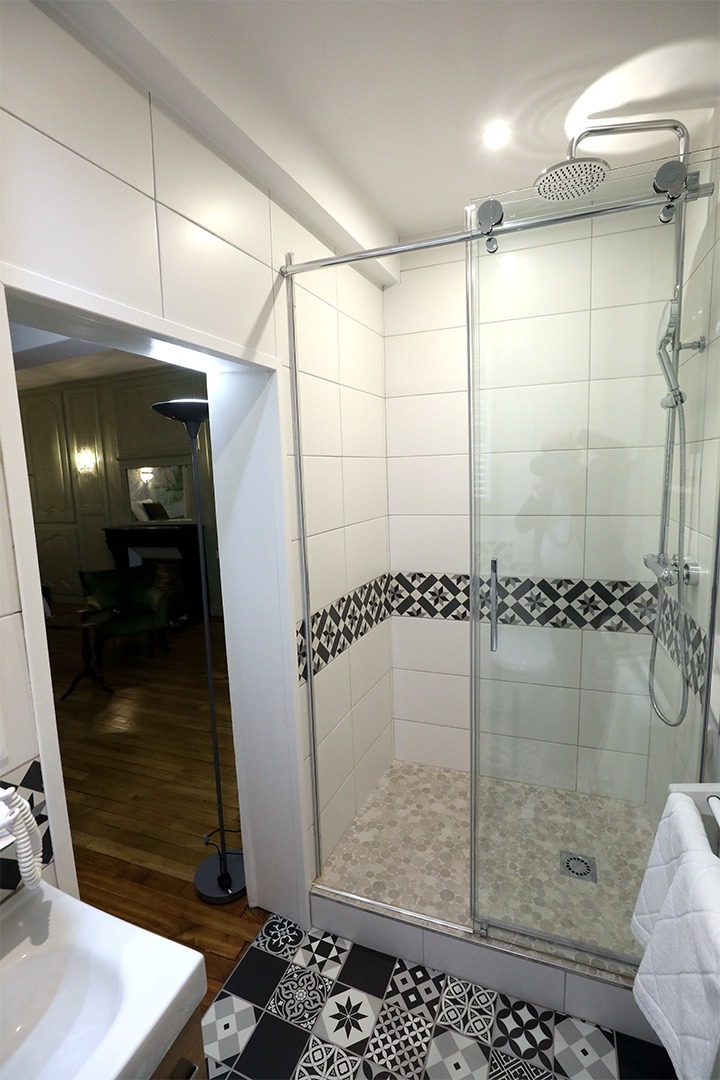 Vue sur la grande douche à l'italienne carrelé en blanc avec un liseré noir à motifs