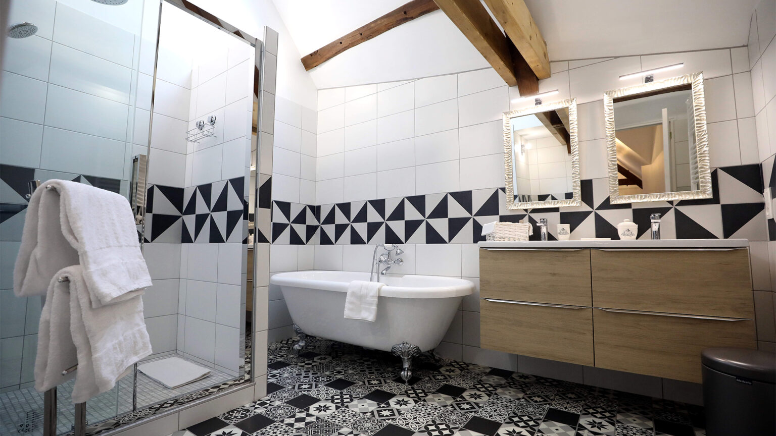 Vue sur la salle de bain qui comprend une grande douche à l'italienne, une baignoire d'époque et son meuble à deux vasque en bois