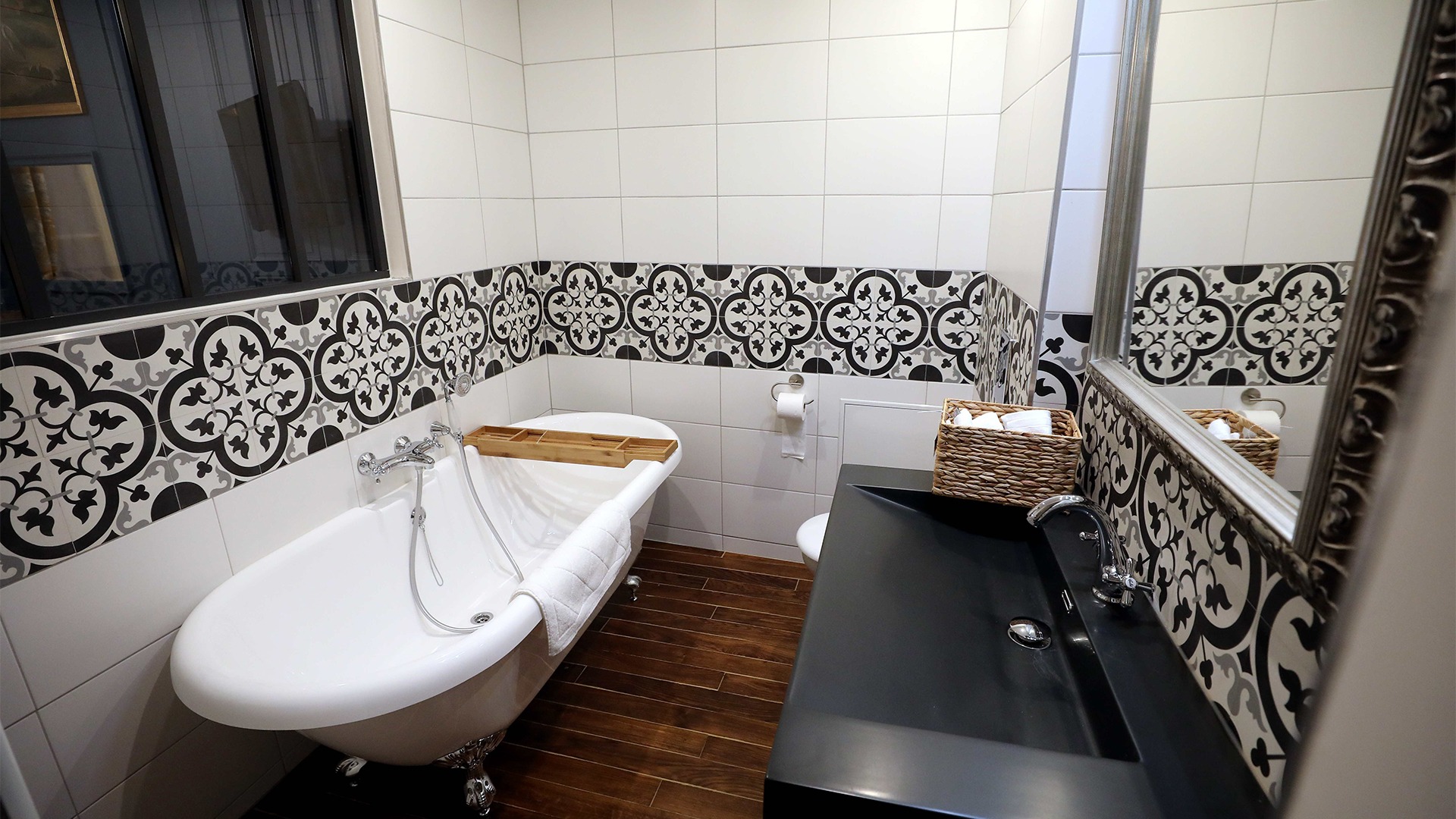 Salle de bain carrelé en blanc avec un liseré à motifs noir, une baignoire d'époque et vasque en pierre noire
