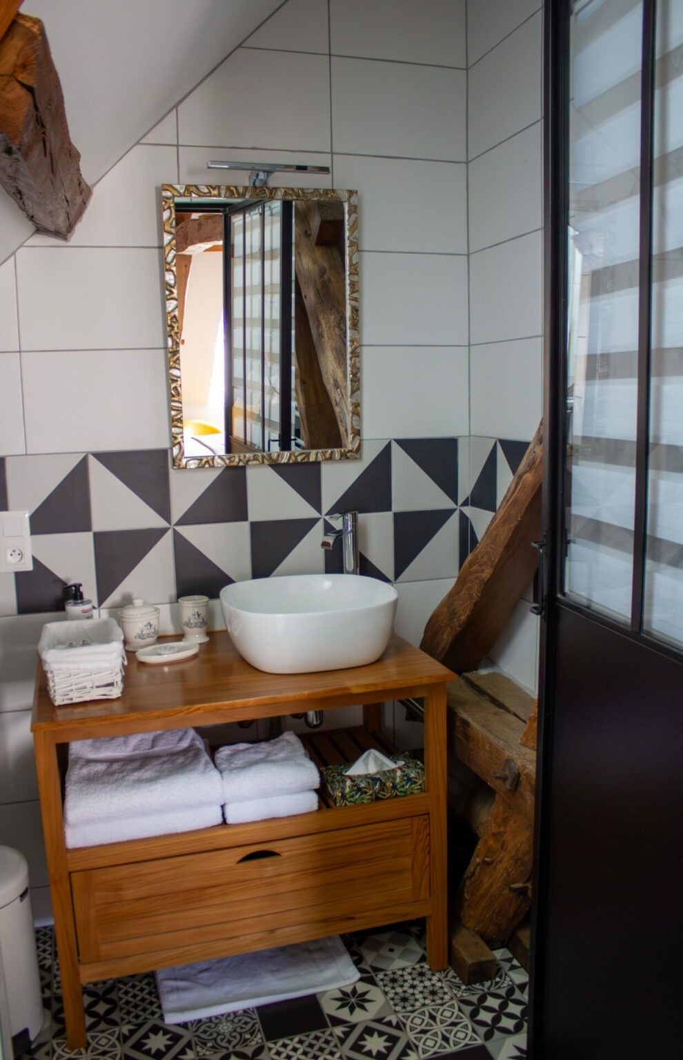Salle de bains en carrelage noir et blanc avec meuble de vasque en bois et poutre apparente